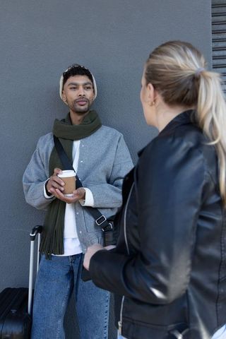 Young travelers chatting on urban street holding coffee cup and rolling suitcase