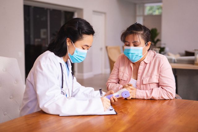 Asian female doctor and patient wearing face masks during medical visit. medicine, health and healthcare services during coronavirus covid 19 pandemic.