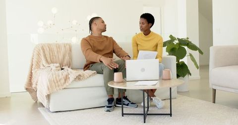 Diverse couple collaborating on couch with laptop and documents