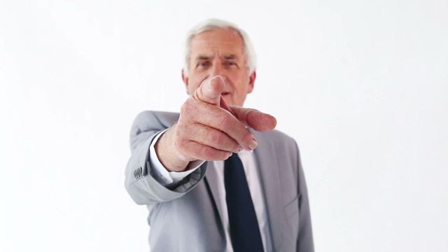 An elderly businessman in a formal suit points directly at the camera with a serious expression. Use this to represent authority, direction, leadership, and decision-making in corporate contexts or motivational content.