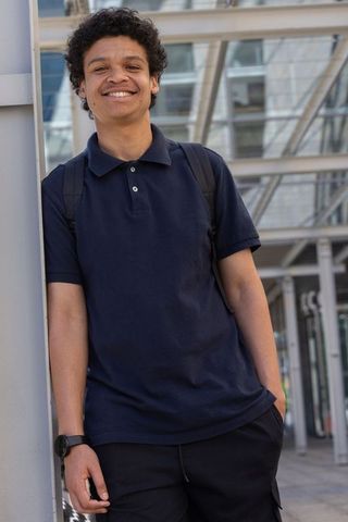 Smiling african american man leaning on column wearing navy polo backpack in urban plaza
