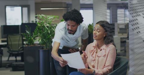 Colleagues reviewing documents and using tablet in modern open-plan office with greenery