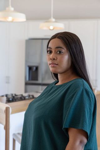 Confident african american woman standing in modern minimalist kitchen by wooden island