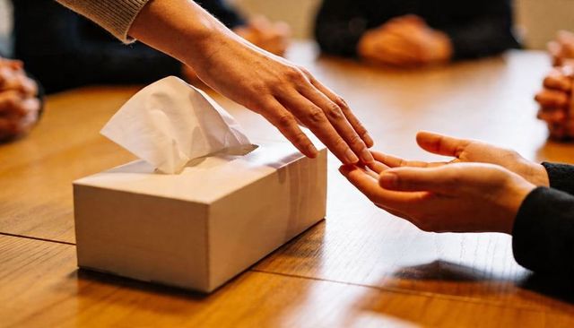 Hands sharing tissue across wooden conference table closeup conveying comfort and support