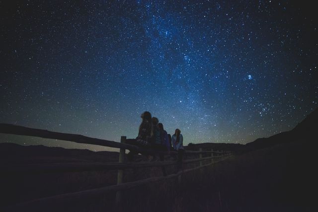 Group of friends enjoying stargazing during the night in the peaceful countryside. Perfect for illustrating themes of friendship, adventure, nature outings, rural tranquility, or nighttime recreation.