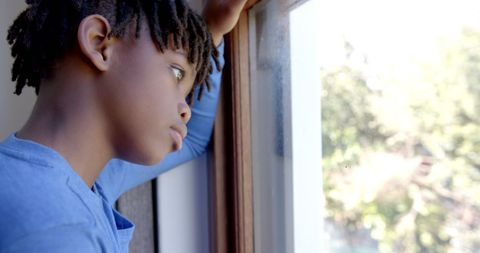 Thoughtful african american boy looking out window in contemplation