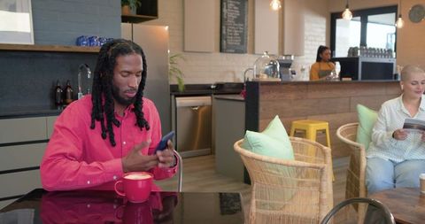 Man checking phone over red latte in modern cafe while companion reading booklet