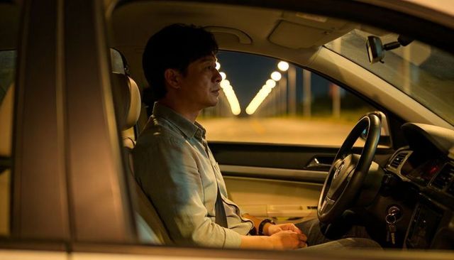 Asian man sitting in parked car at night contemplating under warm streetlight bokeh