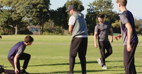 Teenage cricket practice with batsman hitting red ball and fielders chasing in park