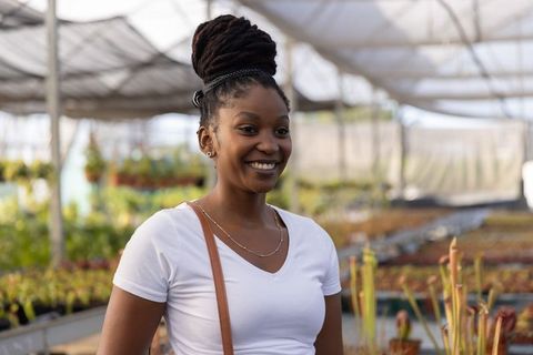 Smiling african american woman browsing greenhouse nursery, inspecting seedlings and plants