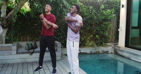 Diverse friends relaxing with arm stretches by poolside deck