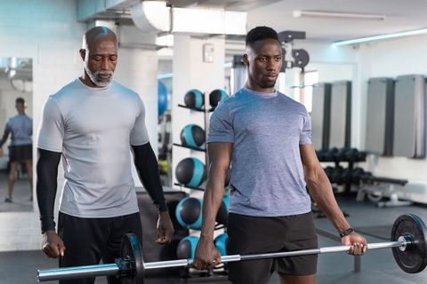African american trainer coaching young athlete performing barbell deadlift in modern gym