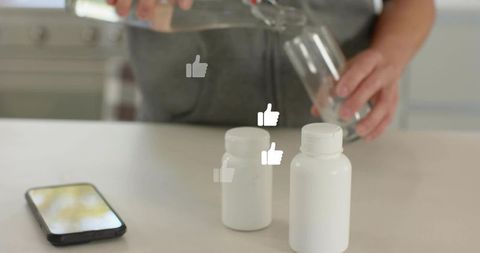 Asian man pouring water into glass next to supplement bottles and smartphone on counter