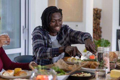 African american man carving roast at cozy family dinner table, smiling and sharing meal with partne