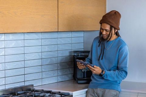 African american man using tablet in modern kitchen leaning on counter with coffee maker