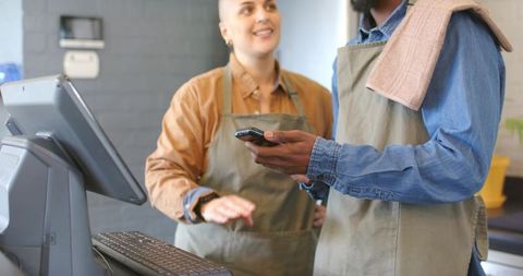 Baristas coordinating orders and mobile payments at pos counter in modern industrial cafe
