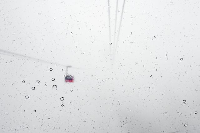 Cable car moving through dense snowy fog viewed through window with raindrops creating abstract overlay. Perfect for weather-related content, transportation themes, winter season promotions, and abstract artistic backgrounds.
