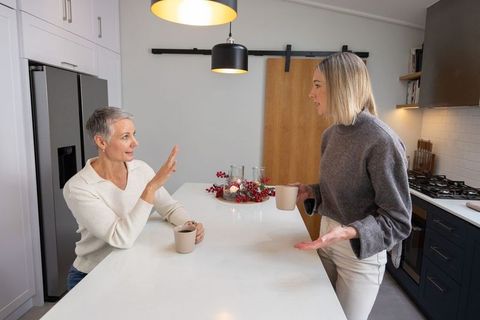 Two women chatting over coffee at modern white kitchen island with pendant lighting