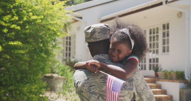 A female soldier, freshly back from deployment, holds her young daughter in a warm embrace outside their home. The daughter is tightly holding onto her mother while clutching an American flag, reflecting themes of family unity, military service, and patriotism. This photo is ideal for portraying the emotional moments involved in military homecomings, family support for military members, and patriotism. It can be effective for use in campaigns supporting military families, Veterans Day promotions, and personal or community stories involving military service.