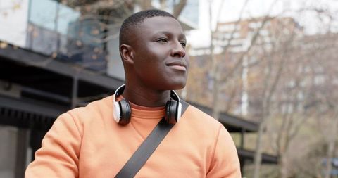 Confident African American man wearing headphones, orange sweatshirt looking right in city
