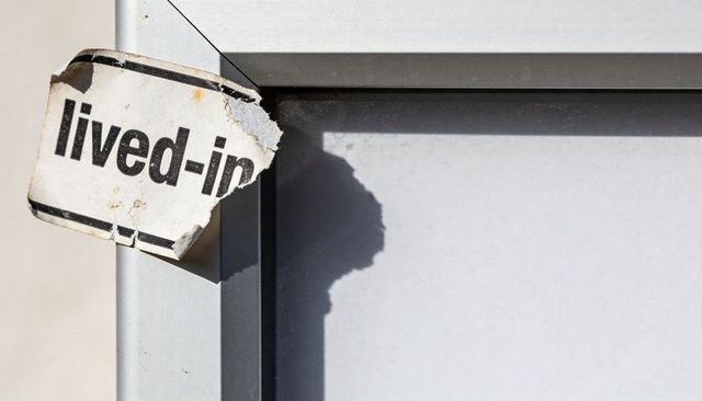 Peeling 'lived-in' sticker on weathered metal frame casting crisp shadow over blank panel