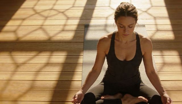Woman meditating in lotus pose on yoga mat with lattice shadows and warm sunlight