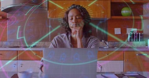 Woman working on laptop in kitchen with holographic interface suggesting remote focus