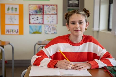 Cheerful Student Writing in Notepad at School Desk