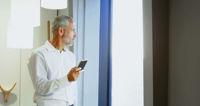 Senior Businessman Looking Outside Window with Smartphone in Hand - Download Free Stock Images Pikwizard.com