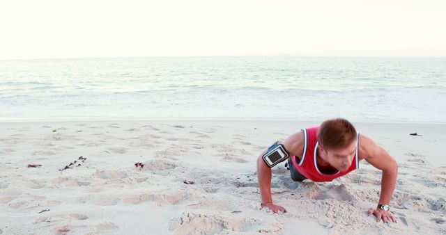 A young Caucasian man is doing push-ups on a sandy beach during sunset, with copy space. His workout routine showcases a commitment to fitness and the serene beach setting provides a tranquil backdrop for exercise.