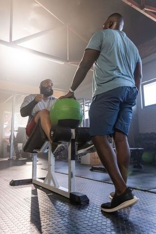 African american men training together at gym on leg ab bench holding green medicine ball