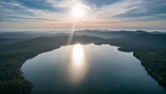 Sunlit mountain lake reflecting low sun over forested peninsula, dock, ridge panorama