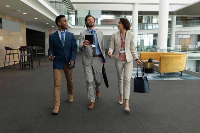 Front view of young multi-ethnic business people interacting with each other while walking on office floor. They are smiiling