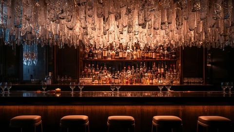 Moody luxury cocktail bar with hanging glass chandelier and glowing back bar warm ambience