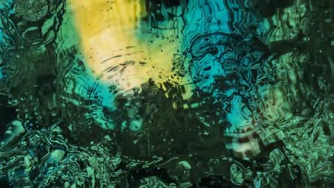 Rippling liquid creating teal and yellow refractions, ripple rings in macro motion