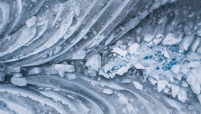 Fractured layered arctic ice field with turquoise crevasse and broken slabs aerial view