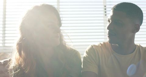 Sunlit couple sharing intimate moment on couch with lens flare and window blinds