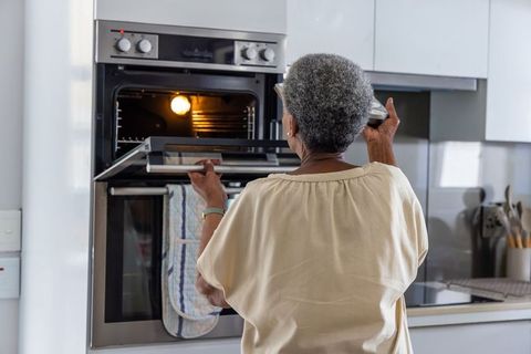 Senior african american woman opening oven and checking dish in modern kitchen
