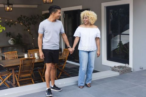 Young couple with african american woman holding hands and smiling on modern patio dining