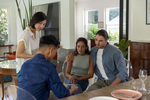 Diverse couple receiving financial advice at home reviewing documents with advisors