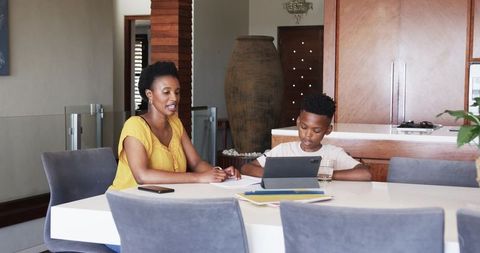 African american mother tutoring son with tablet at dining table in modern kitchen