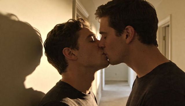 Two men kissing in warm hallway light, intimate gay couple embracing closely