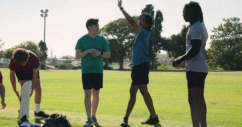 Diverse young men unpacking cricket gear and practicing bowling drills on sunny field
