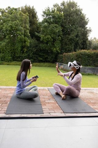 Women practicing yoga while exploring virtual reality meditation on backyard mats