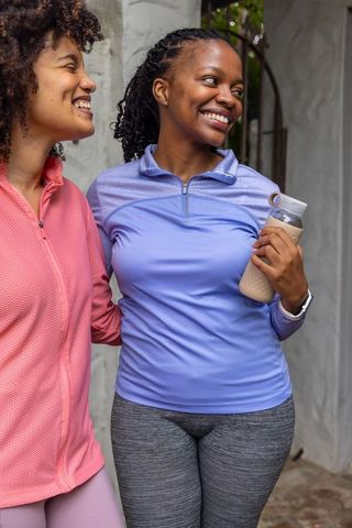 Smiling diverse women hugging after outdoor workout holding water bottle and smartwatch