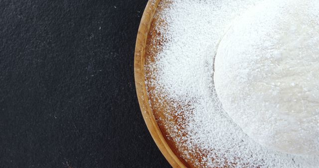A freshly baked cake dusted with powdered sugar sits on a wooden board, with copy space. Its simplicity and the contrast against the dark background suggest a focus on homemade and artisanal baking.
