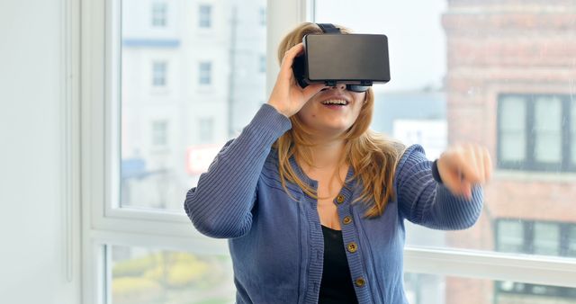Young woman using VR headset, engaged in a virtual experience at home. Excellent for topics related to technology, virtual reality, modern living, and entertainment. Suitable for articles, blogs, or presentations focusing on the impact of VR in daily life.