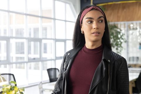 Confident professional woman standing in modern open-plan office wearing leather jacket