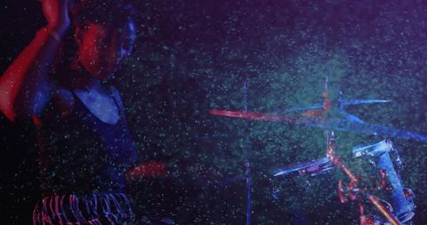 Mid-adult female drummer performing under neon haze with motion blur during rehearsal