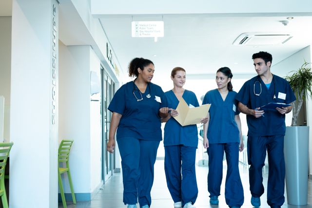 This image shows a diverse group of healthcare professionals, including both female and male doctors, walking and discussing medical files in a hospital corridor. Ideal for use in healthcare-related articles, hospital websites, medical brochures, and advertisements promoting teamwork and diversity in the medical field.